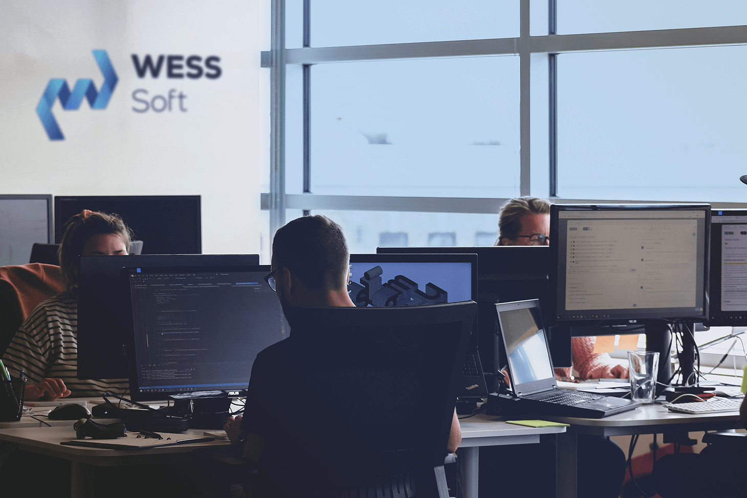 Équipe de développeurs WessSoft travaillant sur ordinateurs avec plusieurs écrans dans un bureau lumineux moderne.