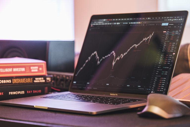 MacBook Pro affichant un graphique boursier à côté de livres d'investissement comme The Intelligent Investor et Principles.